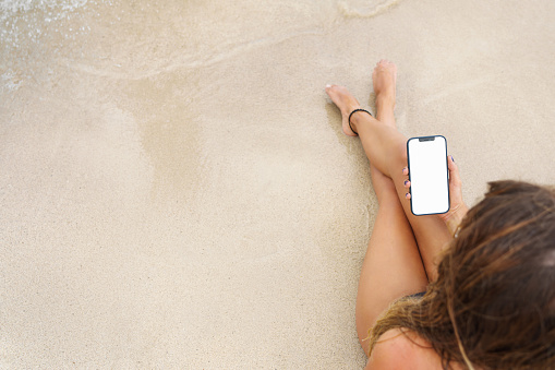 Hand holding the black smartphone with isolated screen and modern frameless design, hold Mobile phone with transparent background at the beach.