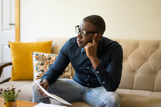 istock Doleful man staring out of window holding utility bills 1473452818