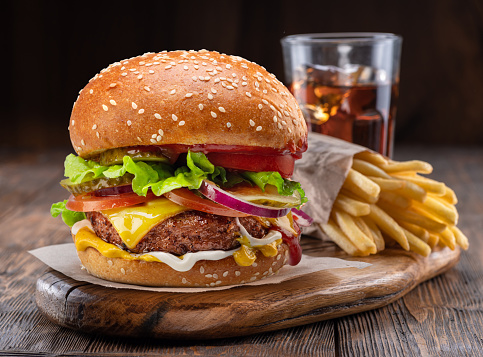 Sabrosa hamburguesa con queso, vaso de cola y papas fritas en primer plano de bandeja de madera. photo