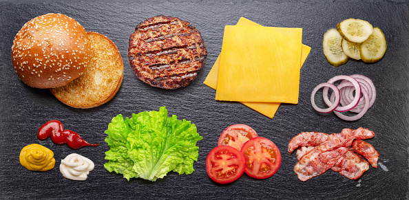 Cheeseburger or hamburger ingredients on natural stone black slate serving plate. Flat lay.