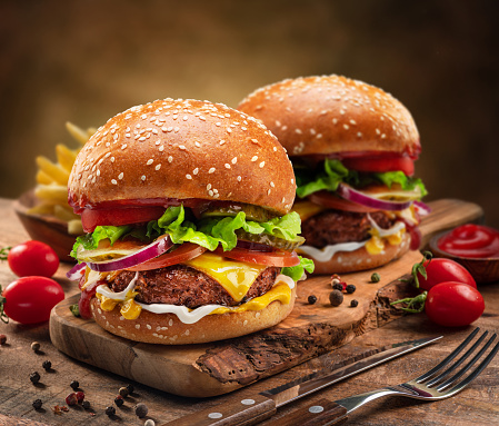 Fresh, tasty and delicious double beef cheeseburger with French fries, tomato, Spanish onion, served  on a plate, bar, restaurant or home kitchen table, close up view with copy space, representing fast food and city life, indulgence and joy through gourmet lifestyle