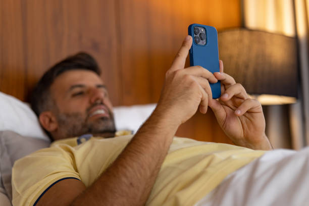 istock Close up of relaxed man using mobile phone on a bed. 1473454410