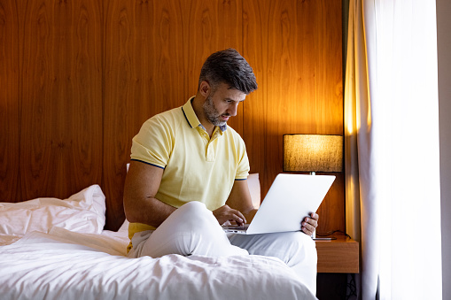 Casual businessman reading an e-mail on a computer while working from his bedroom. Copy space.