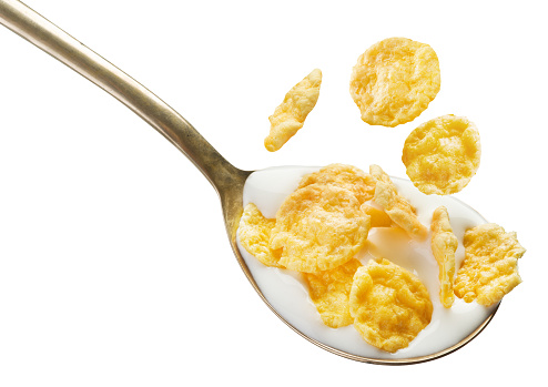 Spoon with milk and cornflakes on white background. File contains clipping path.