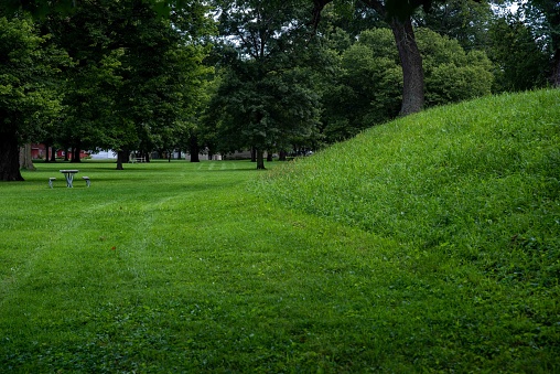 Closeup of sloping exterior of the Great Circle at the Newark Earthworks built by prehistoric indigenous people in Ohio. Empty picnic table in the background. Green grass, sunny outdoors with no people and copy space.
