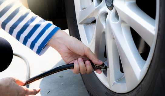Woman inflates the tire. Woman checking tire pressure and pumping air into the tire of car wheel. Car maintenance service for safety before travel. Tire inflating point. Filling air in the tyre of car