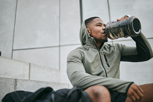 Fitness, relax or black man drinking water in training or exercise for body recovery or workout in Chicago, USA. Hydration, thirsty or tired healthy sports athlete drinks natural liquid in bottle