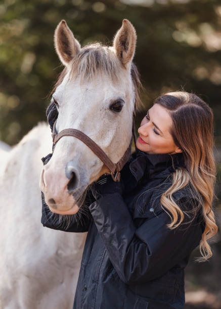 young woman standing next to white arabian horse, blurred trees background, closeup detail - horse arabian horse arabia white imagens e fotografias de stock