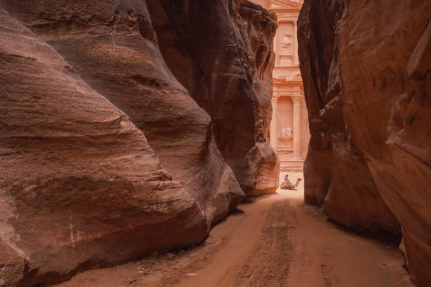 Al Siq Canyon in Petra, Jordan, pink red sandstone walls both sides, unrecognizable person sitting on camel distance, Treasury temple behind stock photo