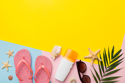 Summer vacation accessories, sunglasses, flip-flops, sunscreen colored background. Traveling essentials flat lay with copy space.