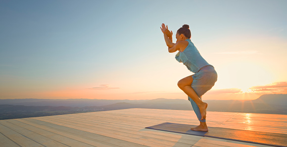 Woman practising garudasana pose yoga on deck during sunset.