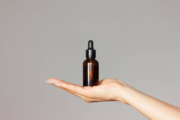 a dark glass bottle with a dropper lid is held in a woman's hand on a light background