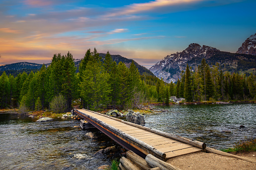Sunset over Taggart Lake and Grand Teton Mountains in Wyoming, USA, with a footbridge in the foreground.