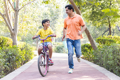Mature father teaching his son to ride bicycle in park.
