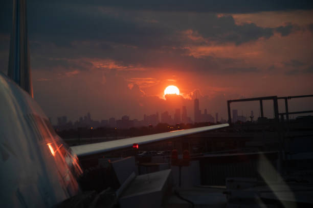 View of red setting sun over Lower Manhattan skyline with airplane and wing visible in the foreground.