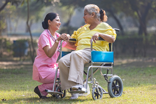 Indian caregiver nurse taking care of senior female patient in a wheelchair at park.