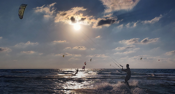 The guy spends active holidays on the sea of Israel at 10.11. 2022 kitesurfing. Kitesurfer parachutes are visible in the background in the distance. on the water in the center of the sun glare in the form of a light path