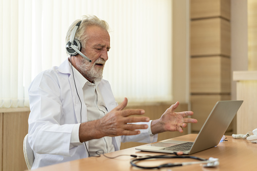 Senior old doctor wears headset. Remote online medical chat consultation, tele medicine distance services. Telehealth concept