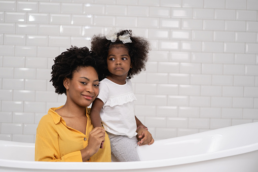 African american family, happy mother and baby daughter having fun and playing together at the bathroom, white wall backgroung