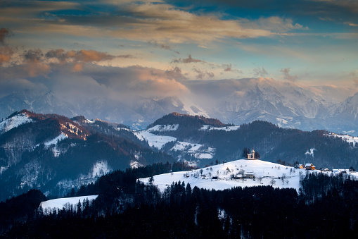 Breathtaking Slovenian sunrise landscape with Julian Alps and charming little church of Sveti Tomaz (St. Thomas) on a hill in winter time, Slovenia