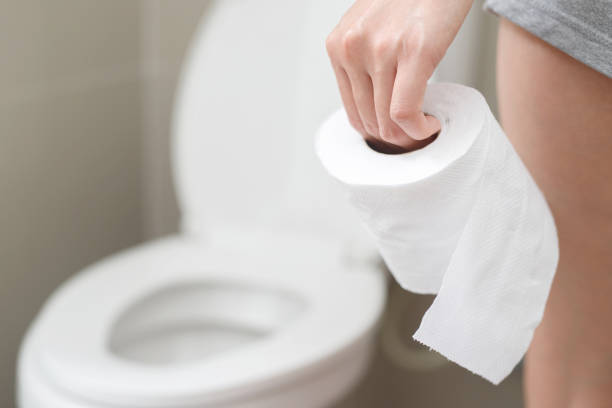 portrait of a woman suffers from diarrhea his stomach painful. ache and problem. hand hold tissue paper roll in front of toilet bowl. constipation in bathroom. hygiene, health care concept. - bacterial mat stockfoto's en -beelden
