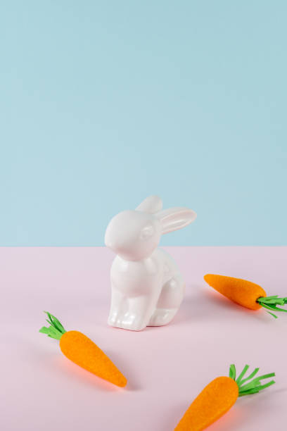 istock White rabbit with carrots on bright background. Minimal pastel pink and blue Easter holiday concept. 1473477170