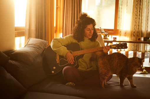 A woman playing guitar in front of cats at home