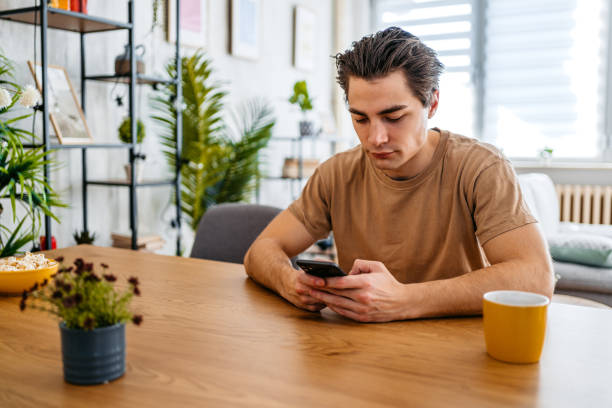 istock Young Man Sitting At The Kitchen Table And Texting On The Phone 1473484936