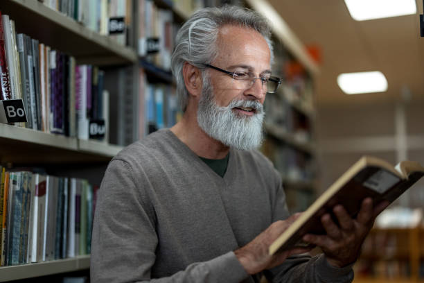 istock Caucasian Retired Man Reading A Book At The City Library 1473485195