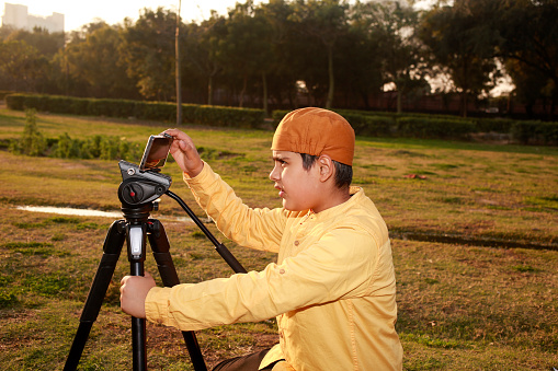 Elementary child of Indian ethnicity setting up mobile phone on tripod in park  for photography and video. Travel photography.
