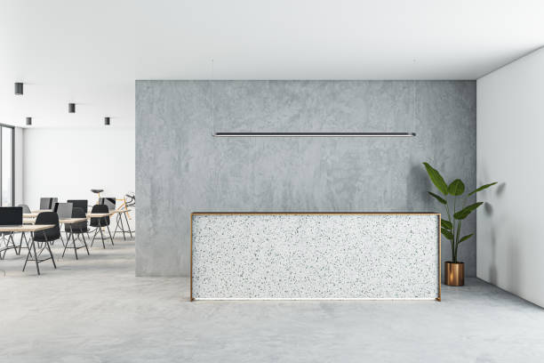 istock Front view on blank reception desk with space for product presentation on light concrete floor, grey wall and coworking office area on background. 3D rendering, mockup 1473487862