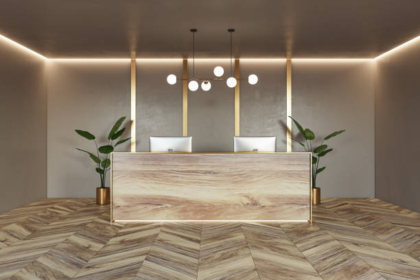 istock Front view on stylish reception desk made from natural wooden slab with modern computers on parquet floor with green plants on beige wall background with lightning on top. 3D rendering 1473494918