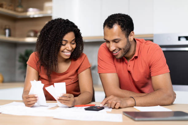 istock Smiling millennial black couple in red t-shirts work with documents, calculate profit, check bills in kitchen interior 1473500855