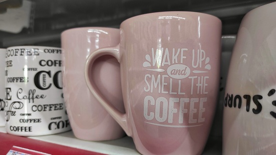 Pink and white ceramic mug with quotes on it displayed on storefront of supermarket to attract the buyer. Can be used for souvenir to drink coffee, tea, or other warm drinks