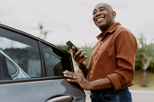 Man getting into car holding smartphone