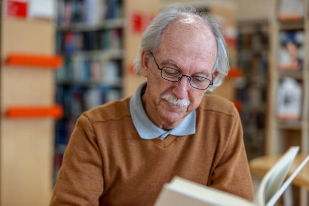 istock Senior Caucasian Man Seated Reading A Book At The Library 1473503532