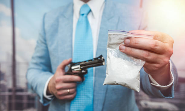 gros plan d’un homme en costume tenant un pistolet et un paquet de drogue cocaïne - narcotic gun medicine currency photos et images de collection
