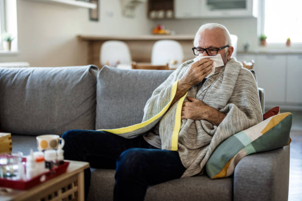 Senior man at home suffering with cold or flu virus. Shot of a senior man blowing his nose with a tissue at home. Senior man at home suffering with cold or flu virus. Shot of a senior man blowing his nose with a tissue at home. cold virus stock pictures, royalty-free photos & images