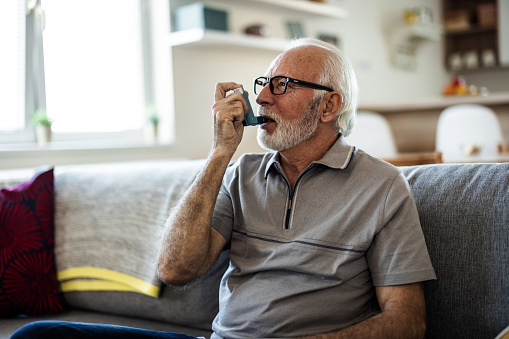 Older man having asthma attack due to his allergies. Mature man using medical inhaler to prevent and treat wheezing and shortness of breath caused by allergy.