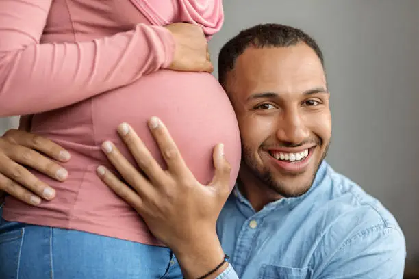 Photo of Happy black man embracing belly of his pregnant muslim wife in hijab