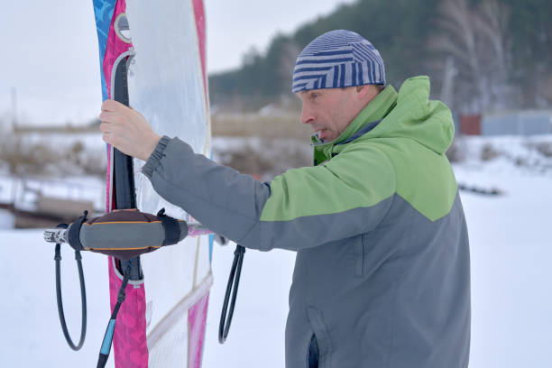 istock Middle-aged man, a snowsurfer, makes the last adjustments on a sail for a sailboard 1473510580