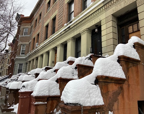 Piles of tall snow form a unique pattern on a row of stepped entrances during a winter storm in Harlem, New York City