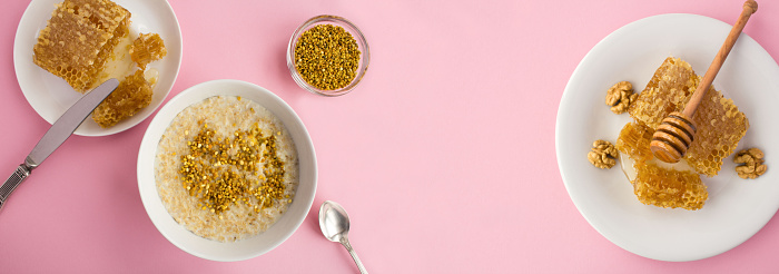 Oatmeal with bee pollen and honey in the white bowl on the pink background. Breakfast. Top view. Copy space.