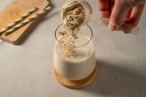 Pouring protein powder from scoop, in glass with milkshake