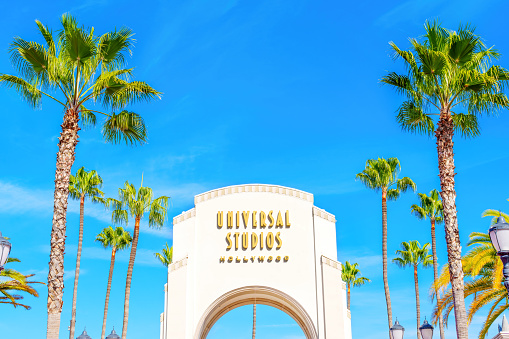 LOS ANGELES, CALIFORNIA - JANUARY 19, 2023: Universal Studios Hollywood Main Entrance Arch With Palm Trees and Blue Sky