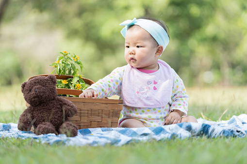 Cute baby sitting on green grass in garden. Asian baby sitting on mat outdoor in park