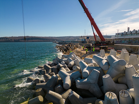 Aerial top view of breakwater construction. Bulldozer and crane on a pile of boulders in the sea