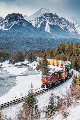 Viewpoint of Morants Curve with iconic red cargo train passing through bow valley and rocky mountains in winter at Banff national park, Alberta, Canada