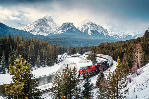 Viewpoint of Morants Curve with iconic red cargo train passing through bow valley and rocky mountains in winter at Banff national park, Alberta, Canada
