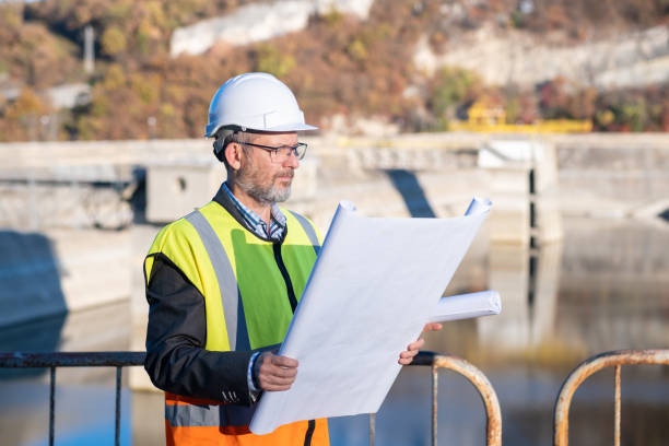 istock A bearded and bespectacled engineer with a blueprint in his hands in front of a dam retaining wall. 1473520132